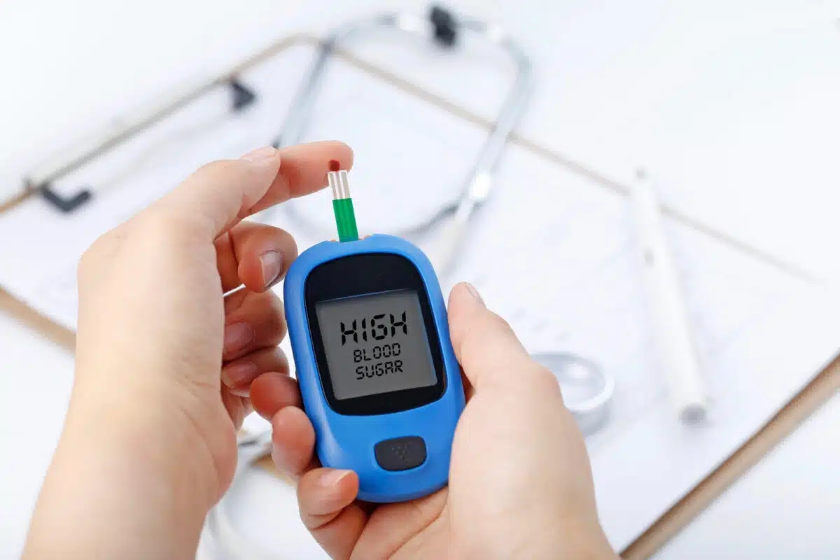 hand-holding-blood-glucose-meter-measuring-blood-sugar-background-is-stethoscope-chart-file